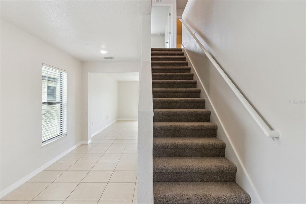 A staircase with brown carpet and a white handrail sits beside a tiled room — 6547 BAIKAL PLACE, LAKELAND, FL