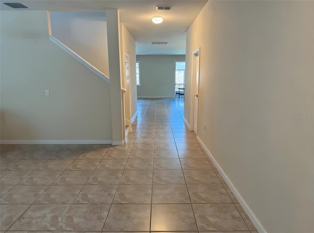 A tiled hallway leads from a staircase toward a bright, open living area — 12109 ECHO BASIN COVE, RIVERVIEW, FL