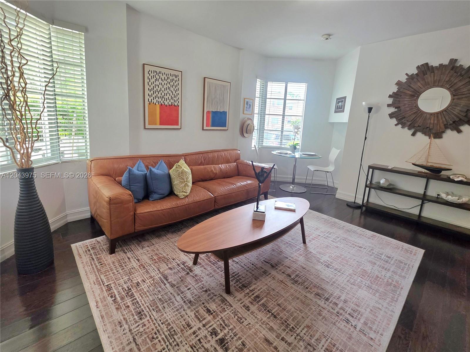 A living room features a brown leather sofa, oval coffee table, and dark wood floors — 601 11th St # 107, Miami Beach FL 33139, MIAMI BEACH, FL