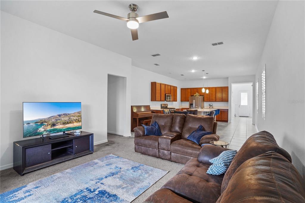 A living room with brown leather sofas, a television, and an open kitchen beyond — 2052 EMERALD SPRINGS DRIVE, APOPKA, FL