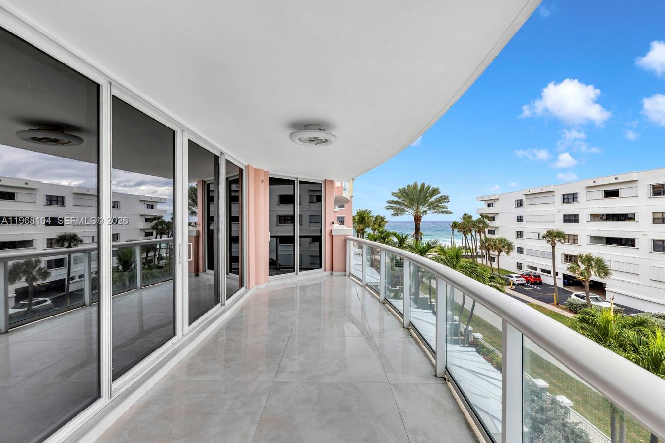A spacious balcony with tile flooring, glass railings, and views of the ocean and buildings — 2051 SE 3rd St # 406, Deerfield Beach FL 33441, DEERFIELD BEACH, FL