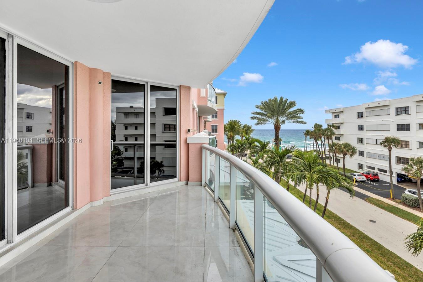 A balcony with tile flooring, glass railings, and a view of palm trees and the ocean — 2051 SE 3rd St # 406, Deerfield Beach FL 33441, DEERFIELD BEACH, FL