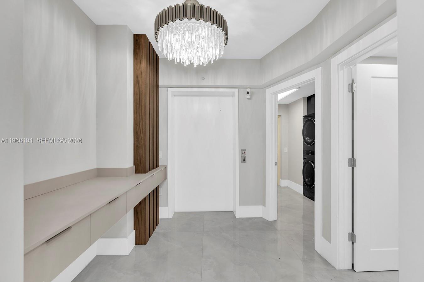 A modern hallway features a crystal chandelier, wood paneling, a floating console, and tile flooring — 2051 SE 3rd St # 406, Deerfield Beach FL 33441, DEERFIELD BEACH, FL