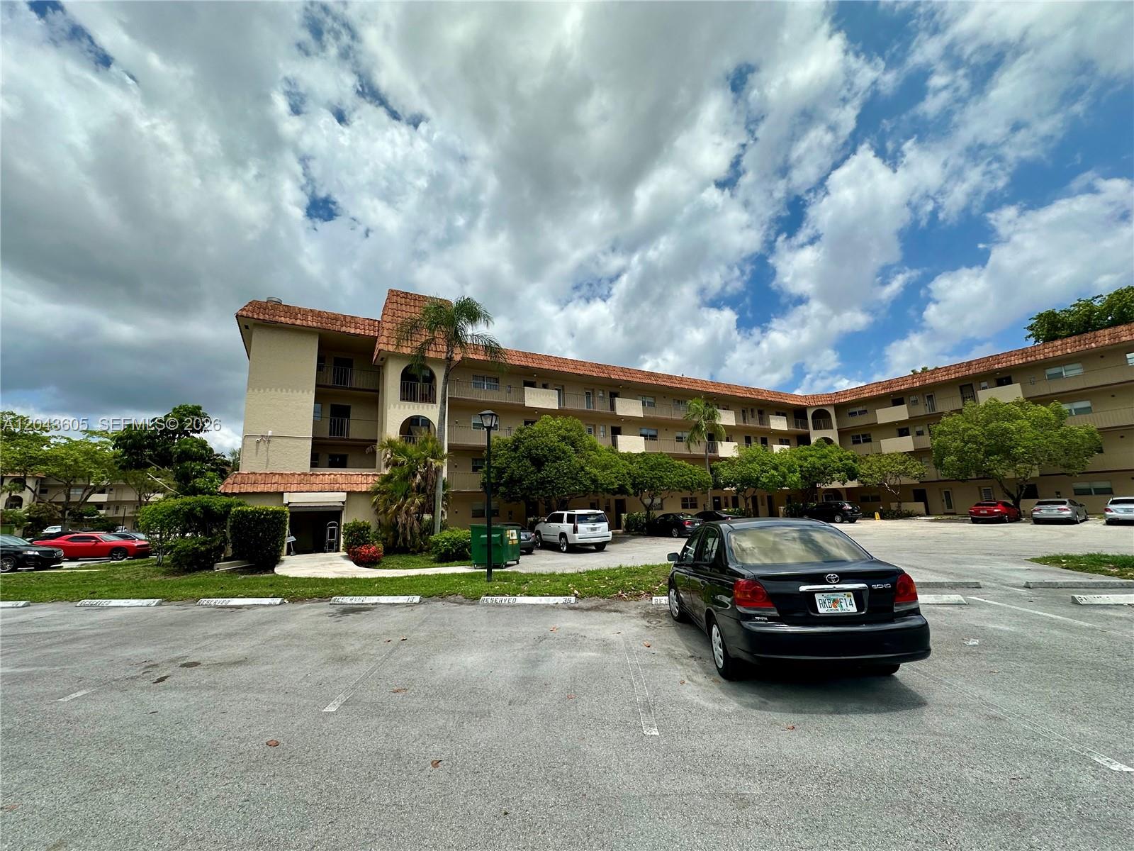 A multi-story apartment building with a tiled roof stands behind a parking lot — 6201 N Falls Cir Dr # 212, Lauderhill FL 33319, LAUDERHILL, FL