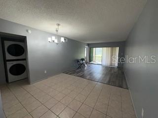 A living room with tile flooring, a stacked washer and dryer, and a sliding glass door — 3269 WESTRIDGE BOULEVARD UNIT 103, ORLANDO, FL