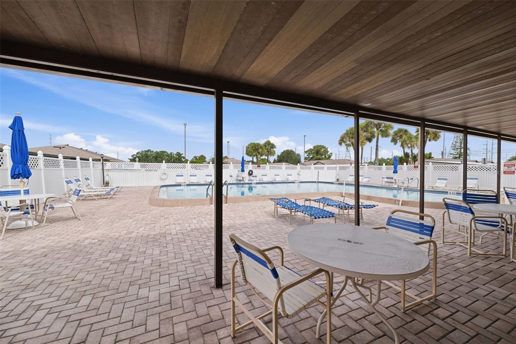 A covered patio with outdoor furniture overlooks a swimming pool surrounded by a white fence — 24862 US HIGHWAY 19 N UNIT 1705, CLEARWATER, FL
