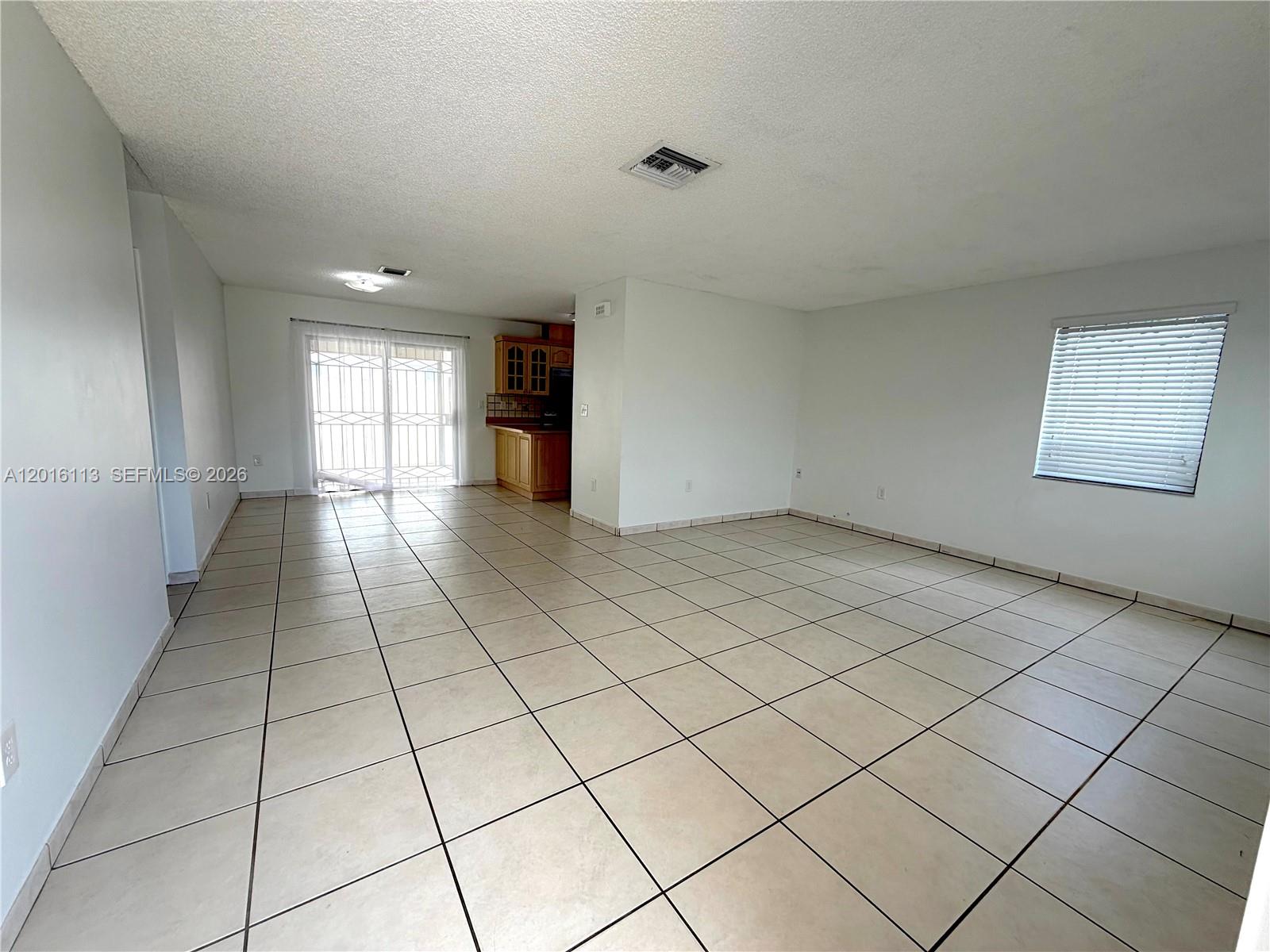 An open-concept living area features light-colored tile flooring, white walls, and a small kitchen — 7993 SW 9th Ter, Miami FL 33144, MIAMI, FL