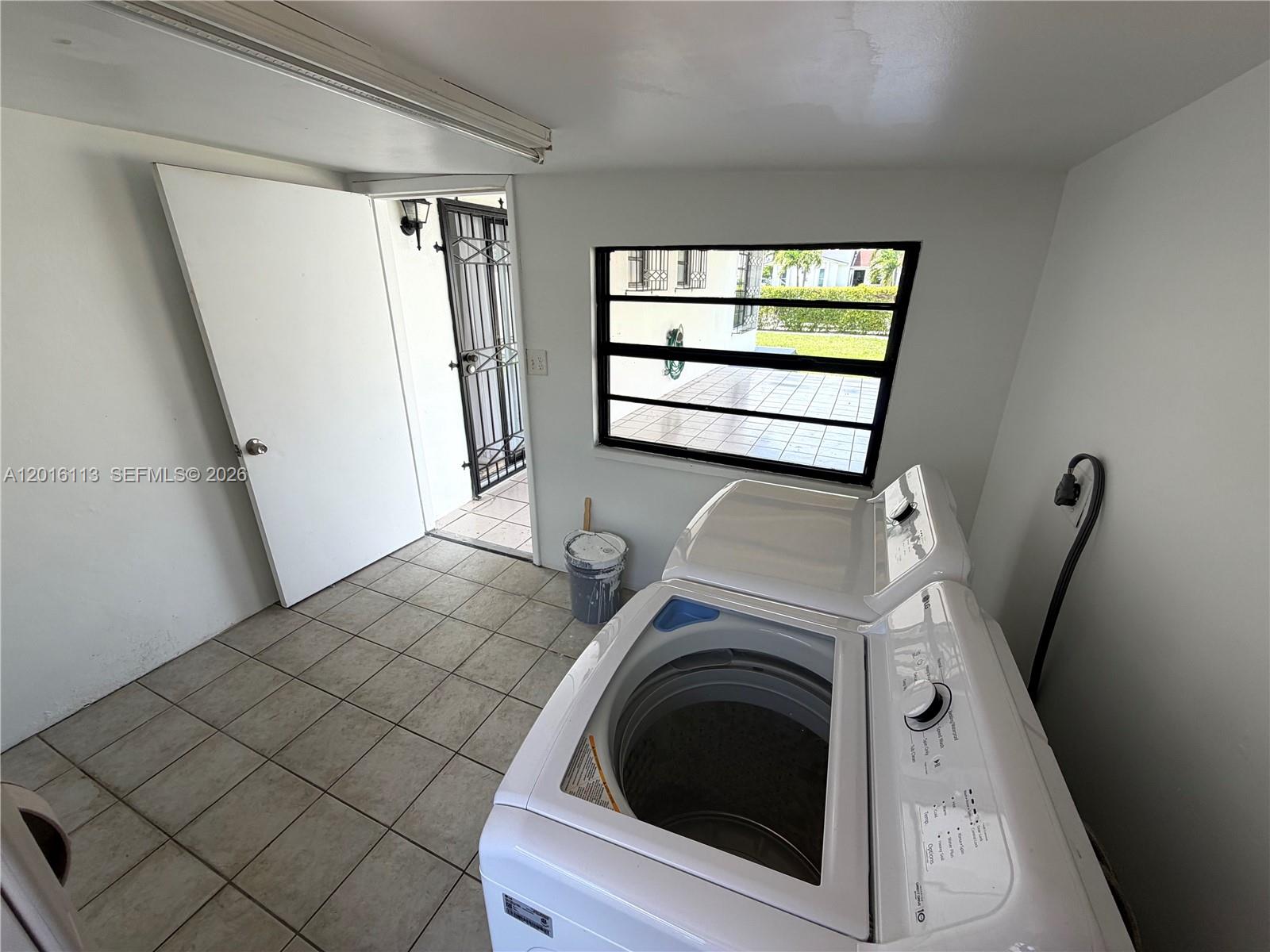 A laundry room with a white washing machine, tiled floors, and a door leading outside — 7993 SW 9th Ter, Miami FL 33144, MIAMI, FL