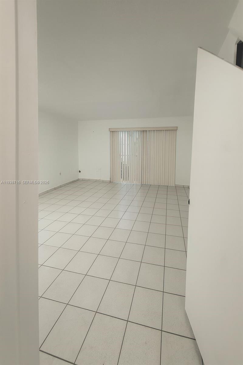 An empty room features white walls, light-colored tile flooring, and vertical blinds over sliding doors — 8170 NW 10th St # 2, Miami FL 33126, MIAMI, FL