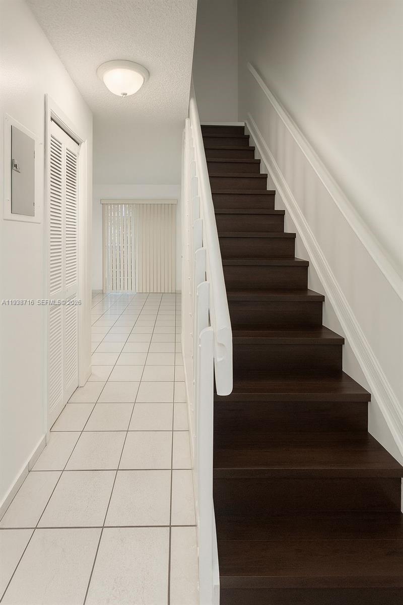 A staircase with dark wood treads leads upward beside a white-tiled hallway — 8170 NW 10th St # 2, Miami FL 33126, MIAMI, FL
