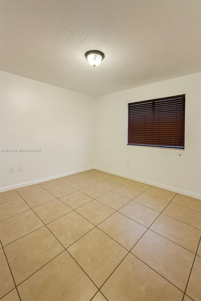 An empty room features beige tile flooring, white walls, and a window with brown blinds — 8170 NW 10th St # 2, Miami FL 33126, MIAMI, FL