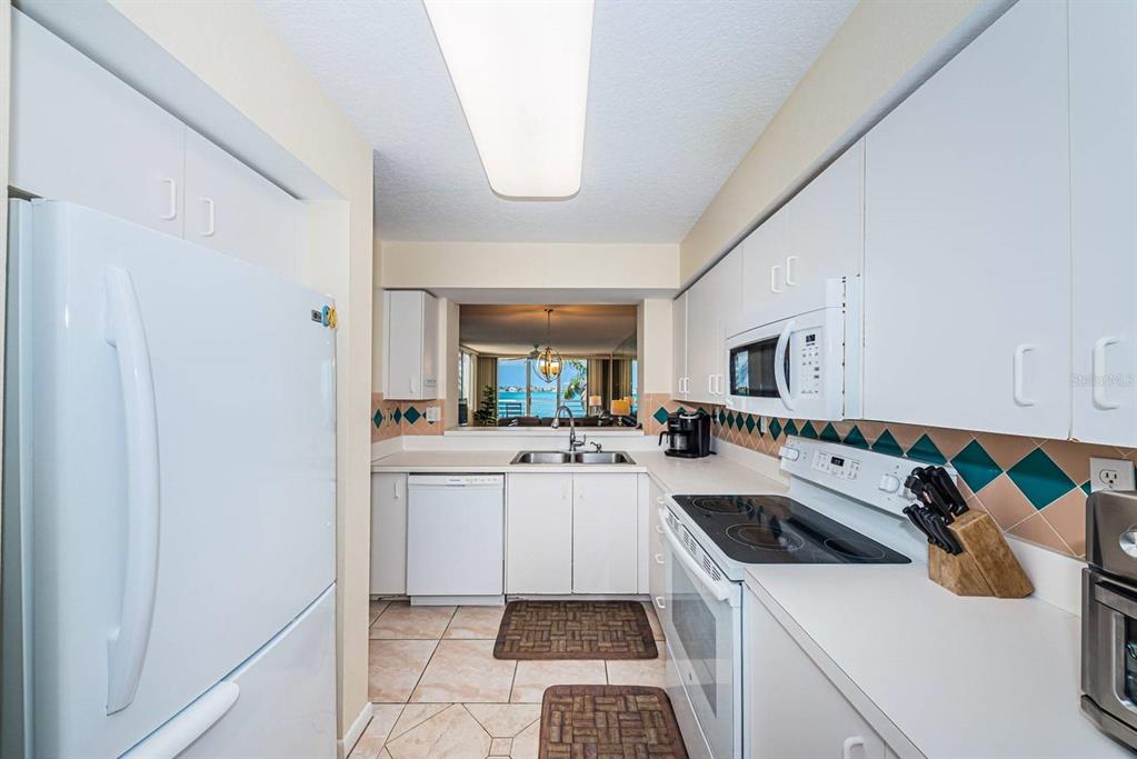 A galley kitchen features white cabinets, white appliances, a tiled backsplash, and a view of water — 6105 BAHIA DEL MAR CIRCLE UNIT 382, ST PETERSBURG, FL