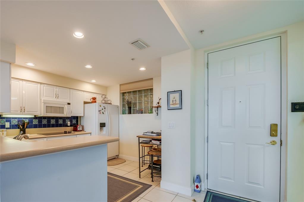 A kitchen with white cabinets and a breakfast bar opens to an entryway with a door — 4624 HARBOUR VILLAGE BOULEVARD UNIT 4504, PONCE INLET, FL