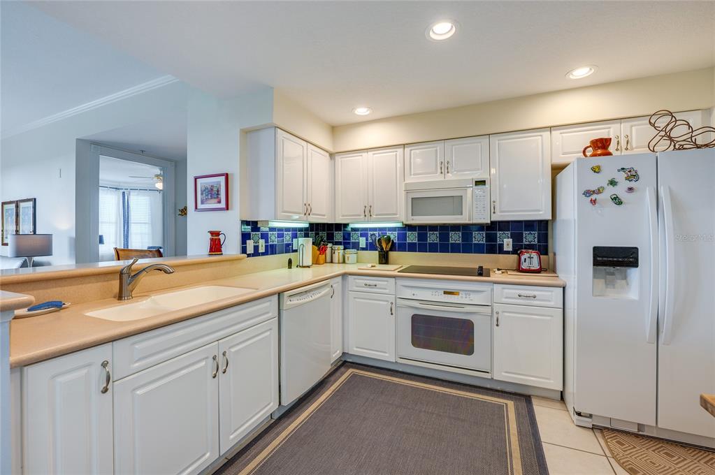 A kitchen with white cabinets, blue tile backsplash, beige countertops, and white appliances — 4624 HARBOUR VILLAGE BOULEVARD UNIT 4504, PONCE INLET, FL