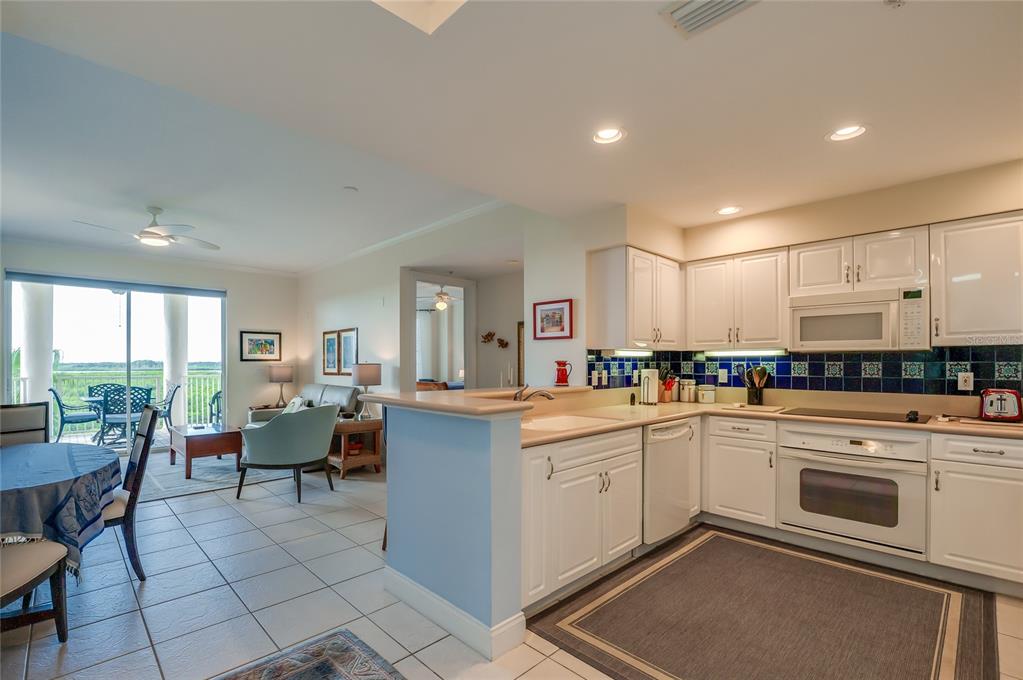A kitchen with white cabinets and blue tile backsplash opens to a living area and balcony — 4624 HARBOUR VILLAGE BOULEVARD UNIT 4504, PONCE INLET, FL
