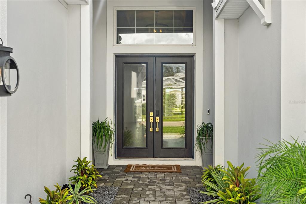 A front entryway features double glass doors, a transom window, and potted plants on pavers — 8761 DRUMMER PLANK DRIVE, WESLEY CHAPEL, FL