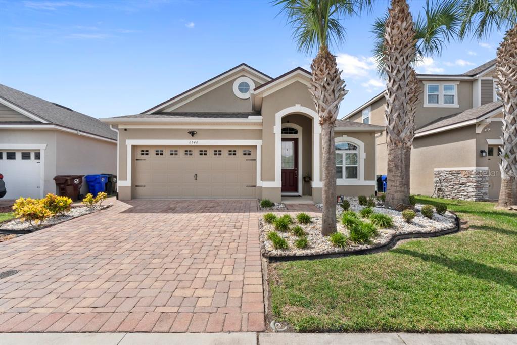 A single-story house with a tan stucco exterior, a paver driveway, and two palm trees — 2542 FOLIO WAY, KISSIMMEE, FL