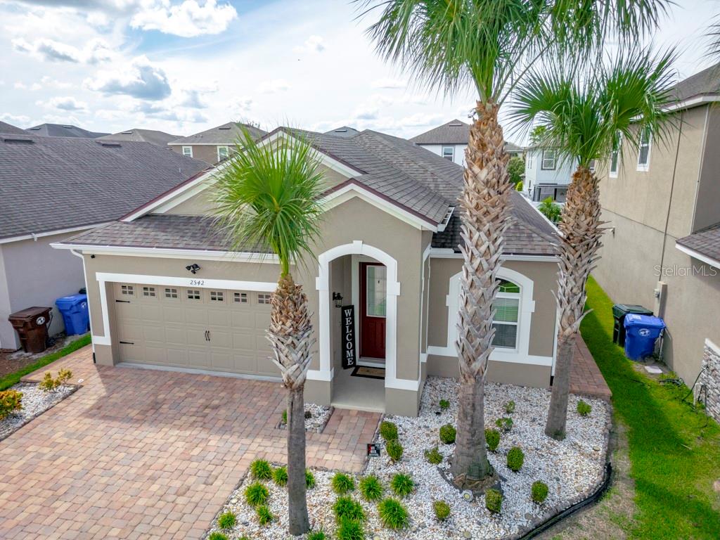 An aerial view shows a single-story house with a tan exterior, a paved driveway, and palm trees — 2542 FOLIO WAY, KISSIMMEE, FL