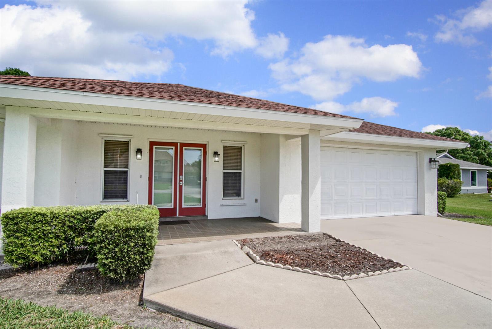 A single-story house with a white stucco exterior, red double front doors, and a garage — 2321 SW 3rd Court, Okeechobee FL 34974, OKEECHOBEE, FL