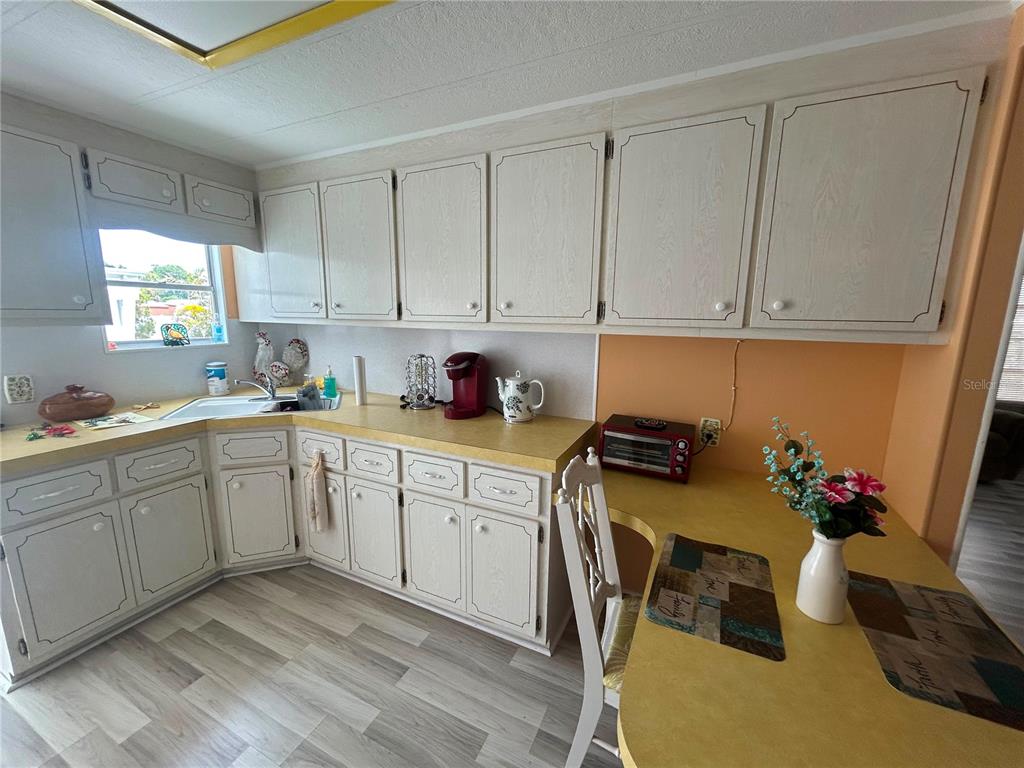 A kitchen features light wood cabinets, yellow countertops, and a small dining area — 7490 46TH AVENUE N UNIT 314, ST PETERSBURG, FL
