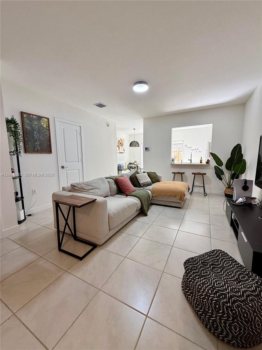 A living room features a large sectional sofa, tile flooring, and a kitchen pass-through window — 487 NE 5th St, Florida City FL 33034, FLORIDA CITY, FL