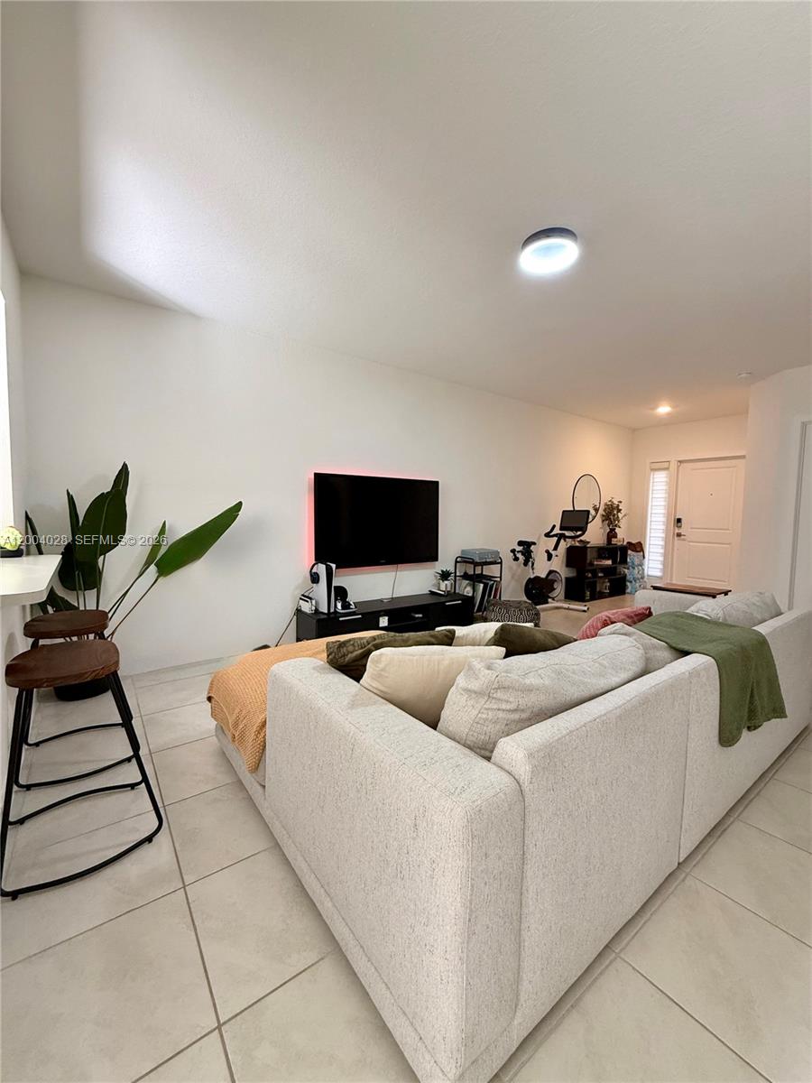 A living room features a light-colored sofa, a wall-mounted television, and a stationary exercise bike — 487 NE 5th St, Florida City FL 33034, FLORIDA CITY, FL