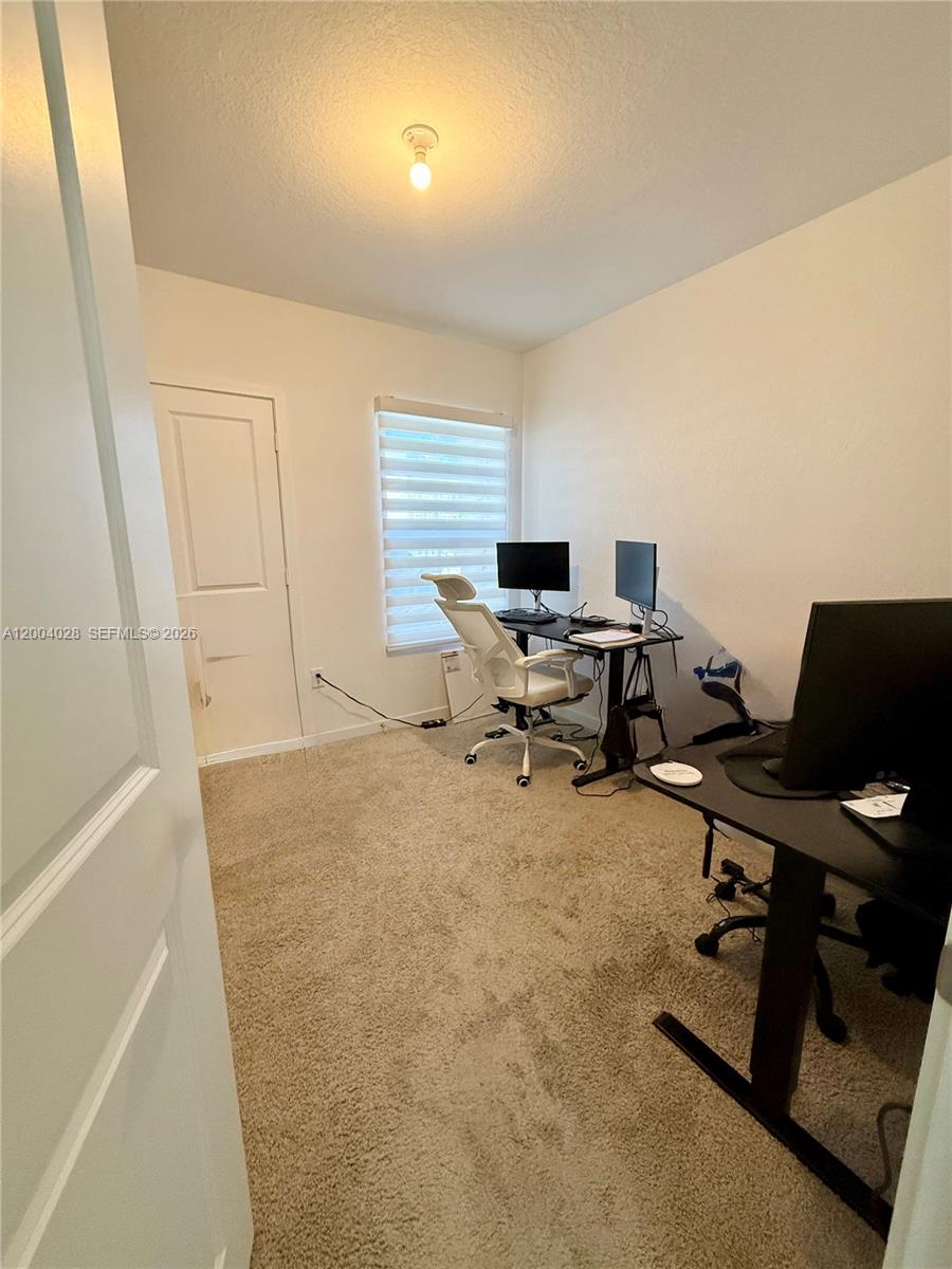 This home office features beige carpeting, two desks, and a window with white blinds — 487 NE 5th St, Florida City FL 33034, FLORIDA CITY, FL