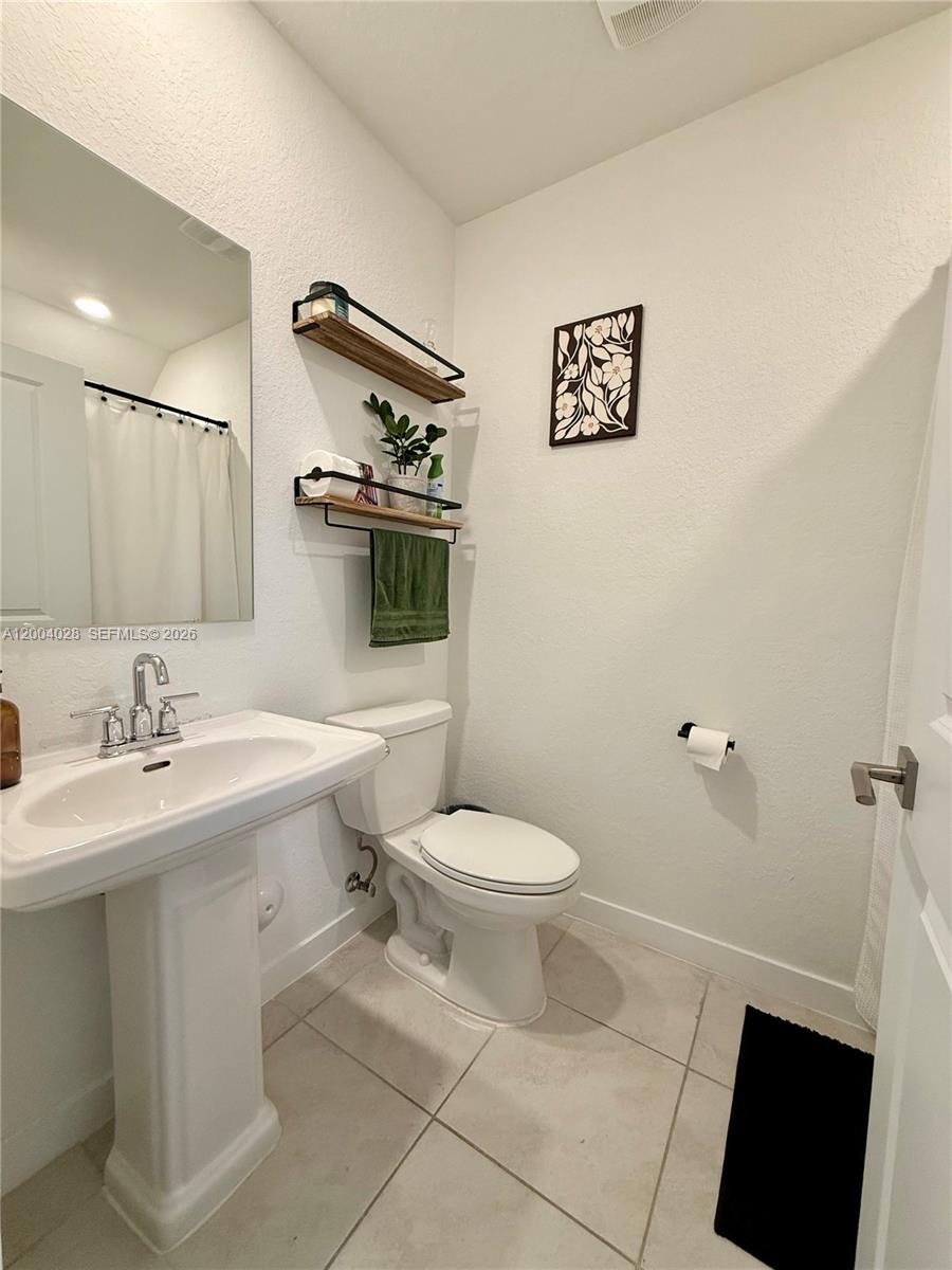 This bathroom features a pedestal sink, a toilet, and two wall-mounted wooden shelves — 487 NE 5th St, Florida City FL 33034, FLORIDA CITY, FL