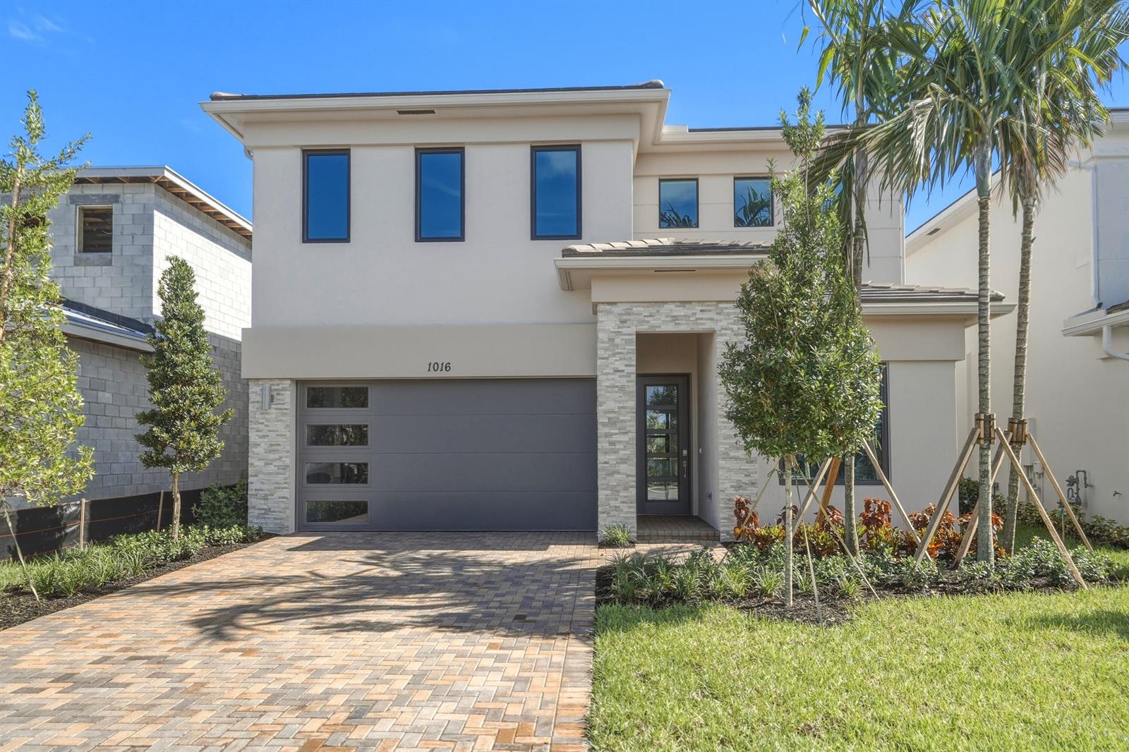 A two-story house with a gray garage door, stone accents, and a brick paver driveway — 1016 Raleigh Way, Wellington FL 33414, WELLINGTON, FL