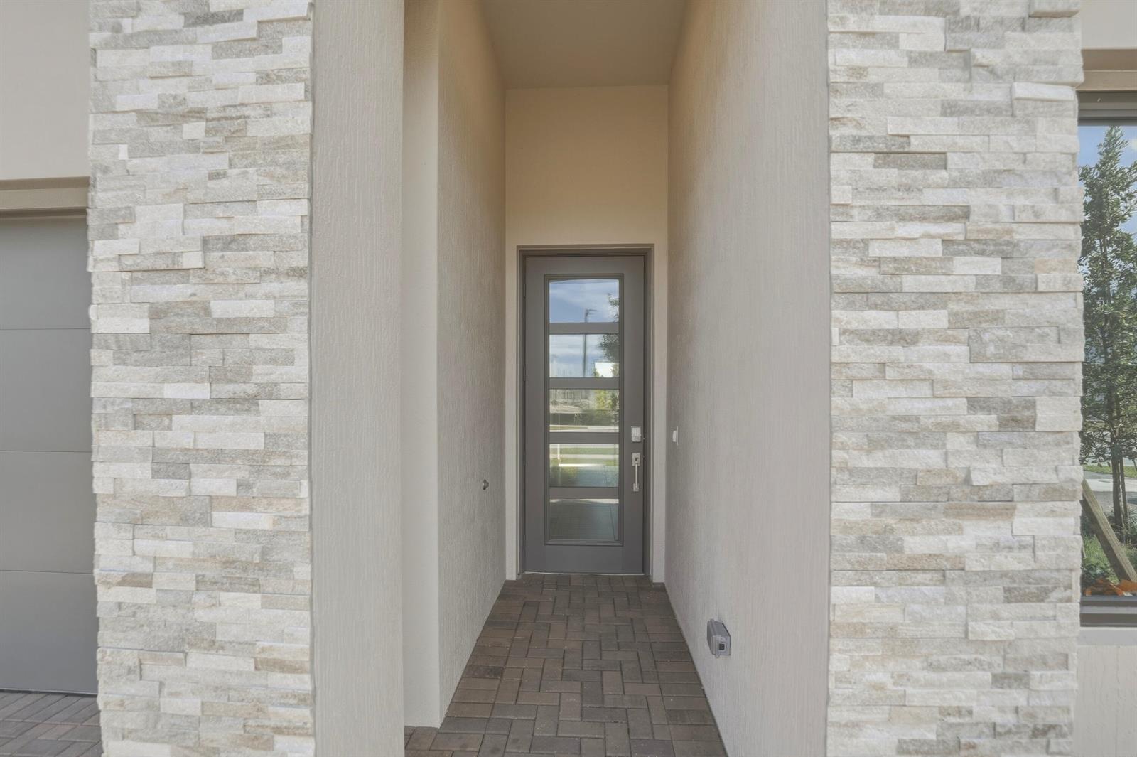 A recessed entryway features a gray door with glass panels, stone veneer, and paver flooring — 1016 Raleigh Way, Wellington FL 33414, WELLINGTON, FL
