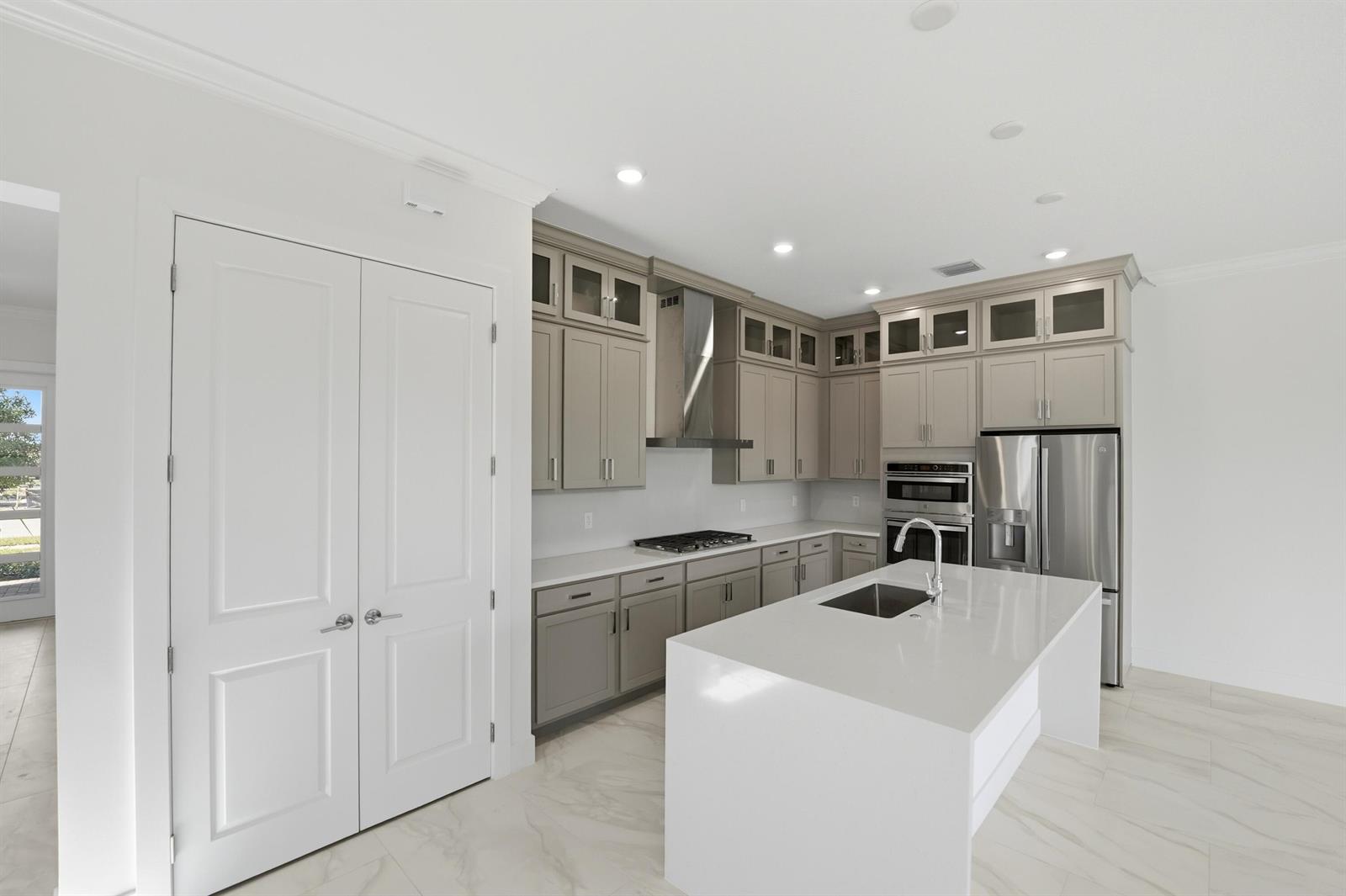 A modern kitchen features gray cabinets, white countertops, stainless steel appliances, and a central island — 1016 Raleigh Way, Wellington FL 33414, WELLINGTON, FL