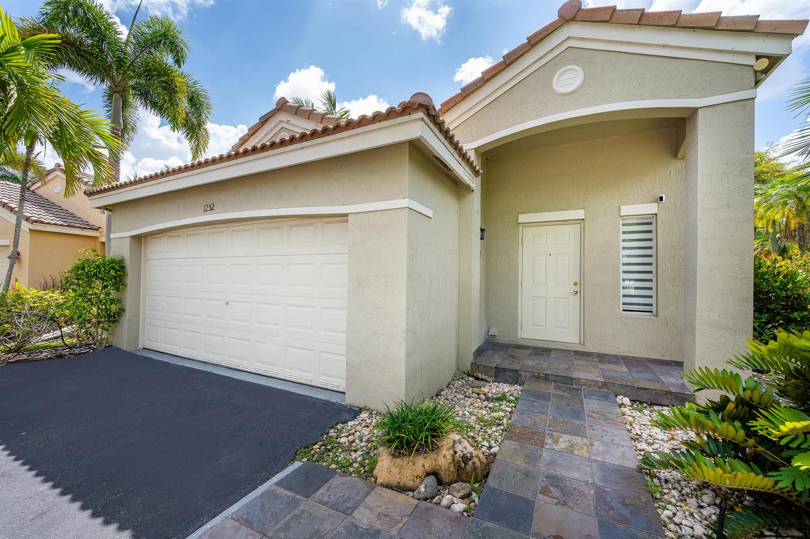 A beige single-story house with a two-car garage, tiled walkway, and a palm tree — 1252 Sabal Trail, Weston FL 33327, WESTON, FL