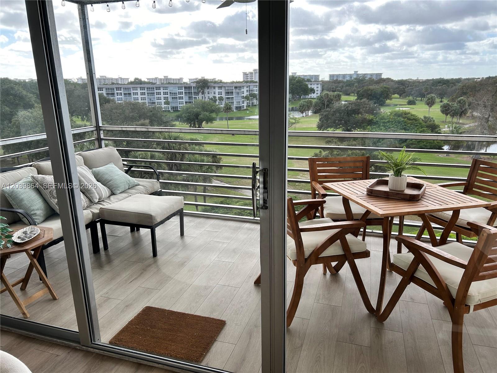 A balcony features wood-look tile flooring, outdoor seating, and a view of a golf course — 3520 Oaks Way # 607, Pompano Beach FL 33069, POMPANO BEACH, FL