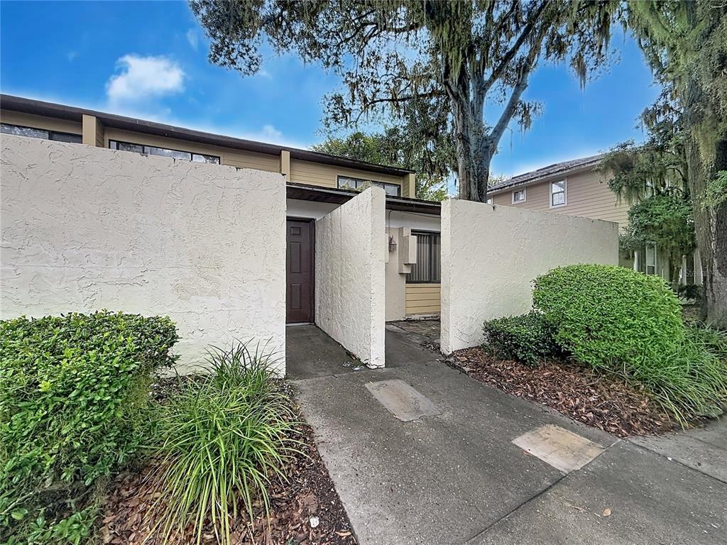 A brown front door is recessed between two white stucco privacy walls on a walkway — 2508 SW 35TH PLACE UNIT A6, GAINESVILLE, FL