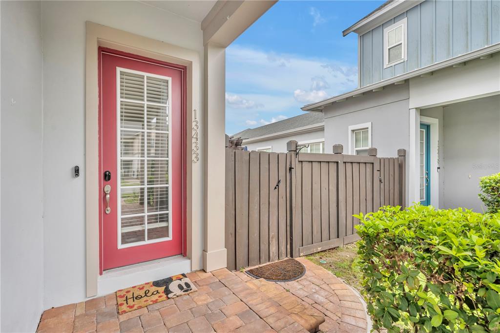 A red front door with a glass insert sits beside a wooden privacy fence — 13433 STODDART AVENUE, ORLANDO, FL