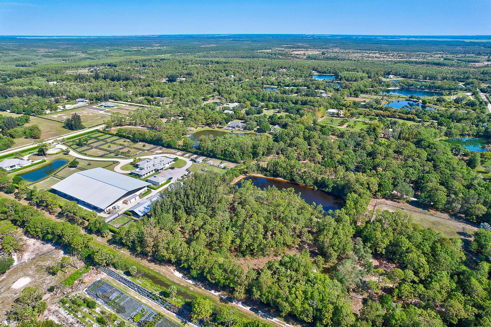 An aerial view shows a large equestrian estate with a covered arena, stables, and ponds — 18395 131st Trail N, Jupiter FL 33478, JUPITER, FL