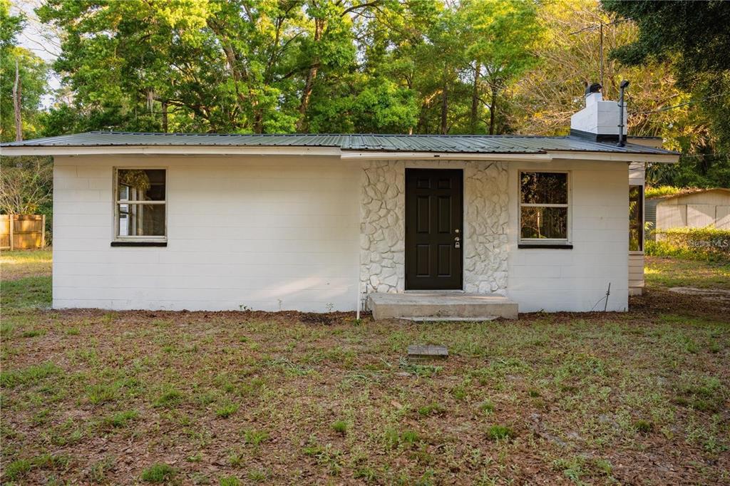 A single-story white concrete block house with a dark metal roof and a black door — 107 EARLS LANE, APOPKA, FL