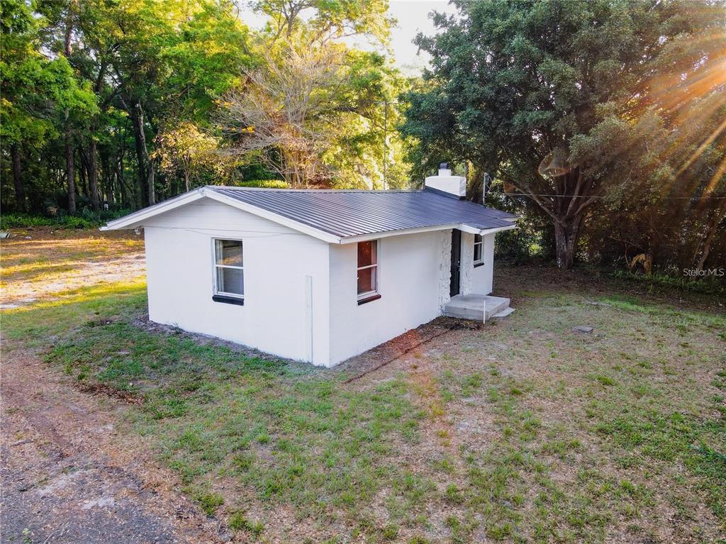 A small, white, single-story house with a dark metal roof sits on a grassy lot — 107 EARLS LANE, APOPKA, FL