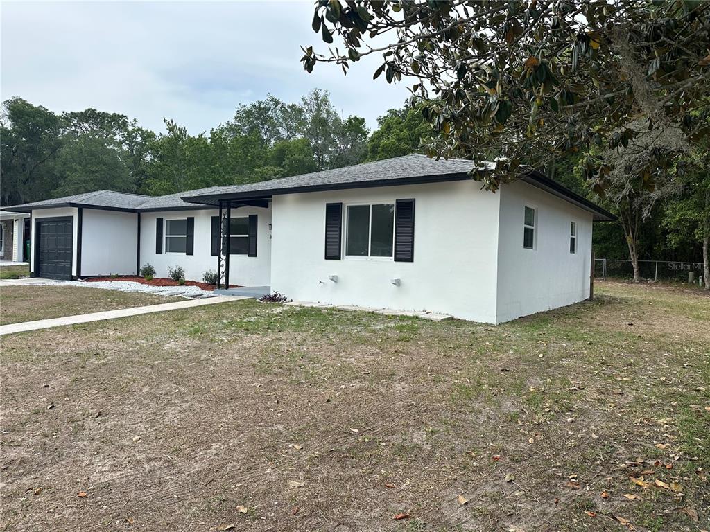 A white single-story house with a black roof, dark shutters, and an attached garage — 9330 N CITRUS SPRINGS BOULEVARD, CITRUS SPRINGS, FL