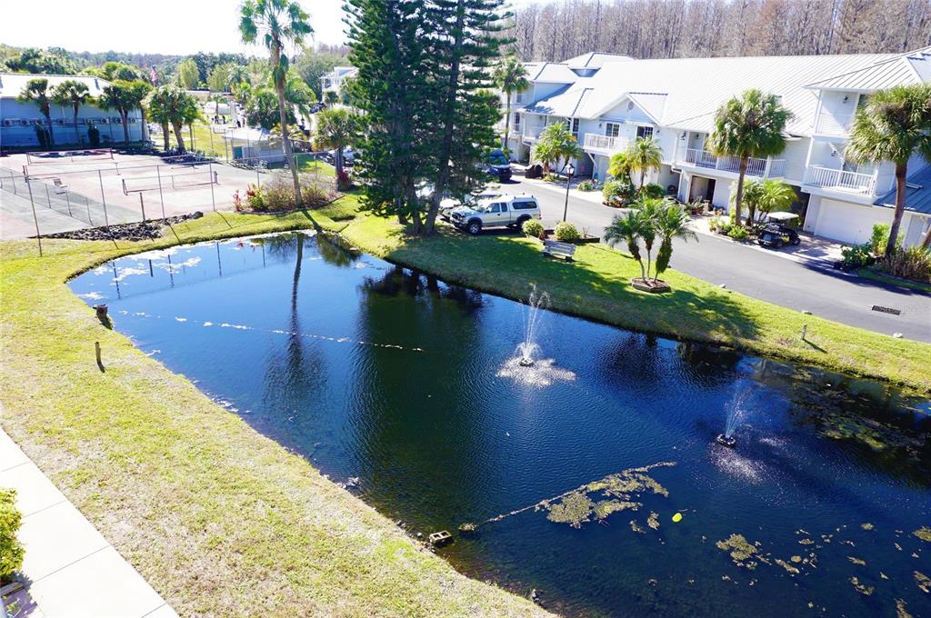 An aerial view of a pond with fountains, tennis courts, and multi-story residential buildings — 2210 VISTA DEL SOL CIRCLE UNIT 520, LUTZ, FL