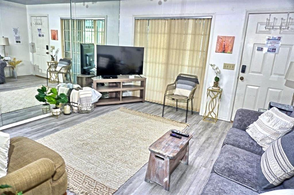 A living room features gray wood-look flooring, a large mirror, and a television on a stand — 2210 VISTA DEL SOL CIRCLE UNIT 520, LUTZ, FL