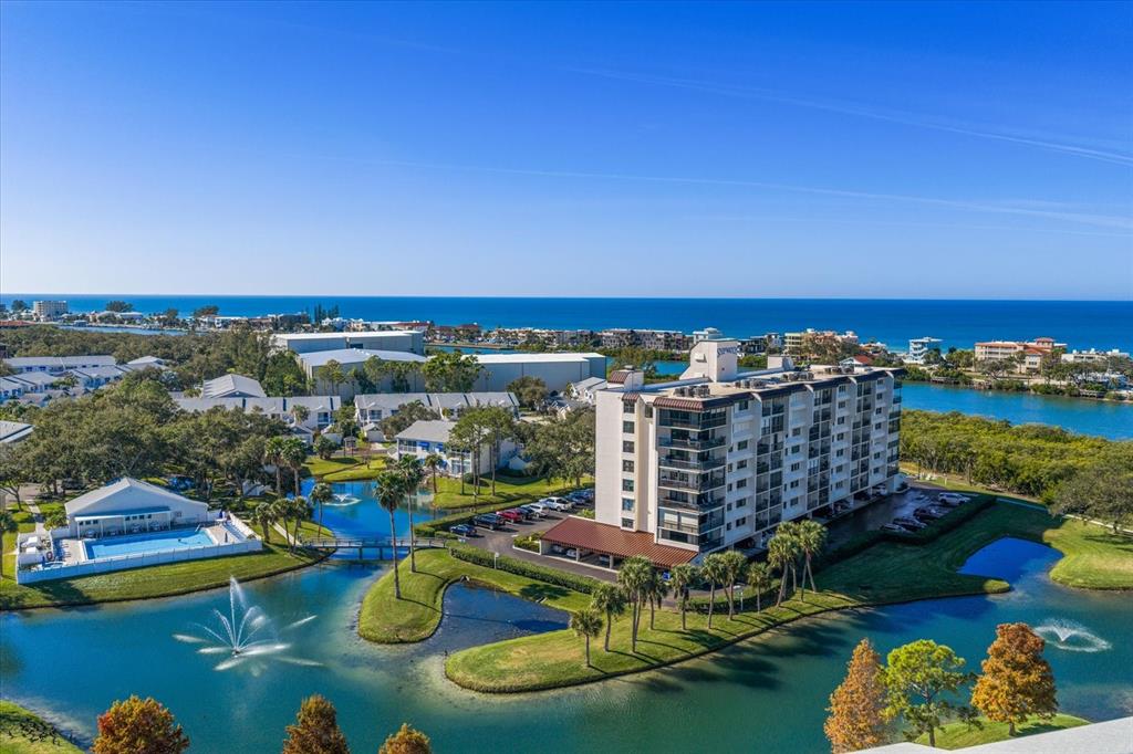 An aerial view shows a multi-story apartment building surrounded by ponds, palm trees, and water — 11590 SHIPWATCH DRIVE UNIT 447, LARGO, FL