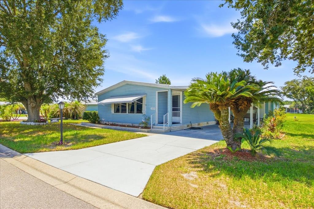 A light blue mobile home features a concrete driveway, a palm tree, and mature trees — 2679 LAKE GRASSMERE CIRCLE UNIT 903, ZELLWOOD, FL