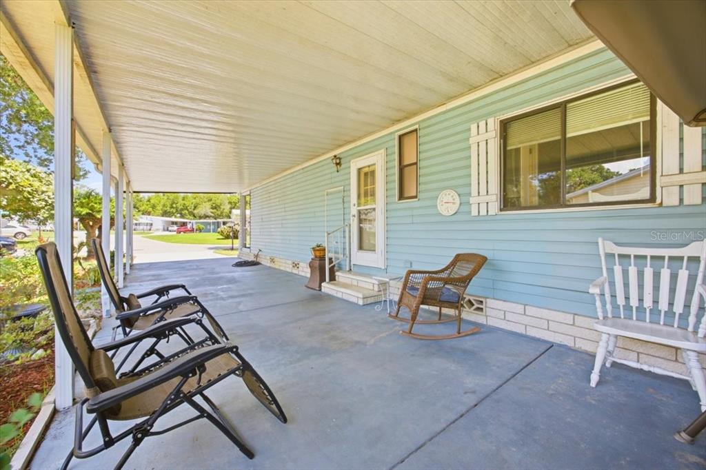 A covered concrete patio features light blue siding, a white door, and several outdoor chairs — 2679 LAKE GRASSMERE CIRCLE UNIT 903, ZELLWOOD, FL