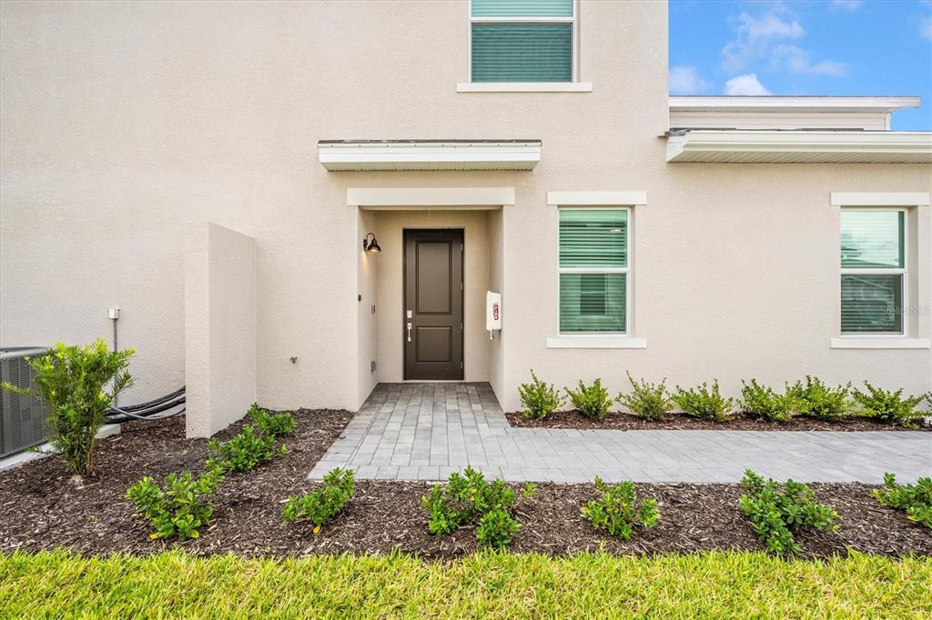 The exterior of a beige two-story house features a dark front door and paved walkway — 12620 RADIANCE COURT UNIT 101, VENICE, FL