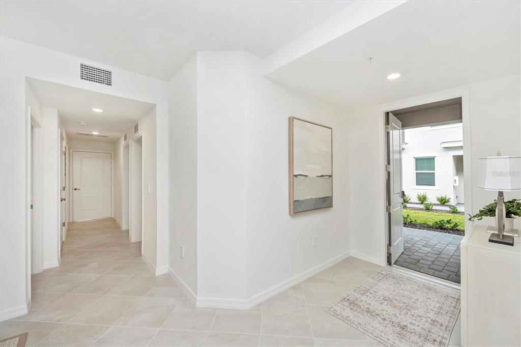 A bright entryway features light tile floors, a framed wall painting, and an open front door — 12620 RADIANCE COURT UNIT 101, VENICE, FL