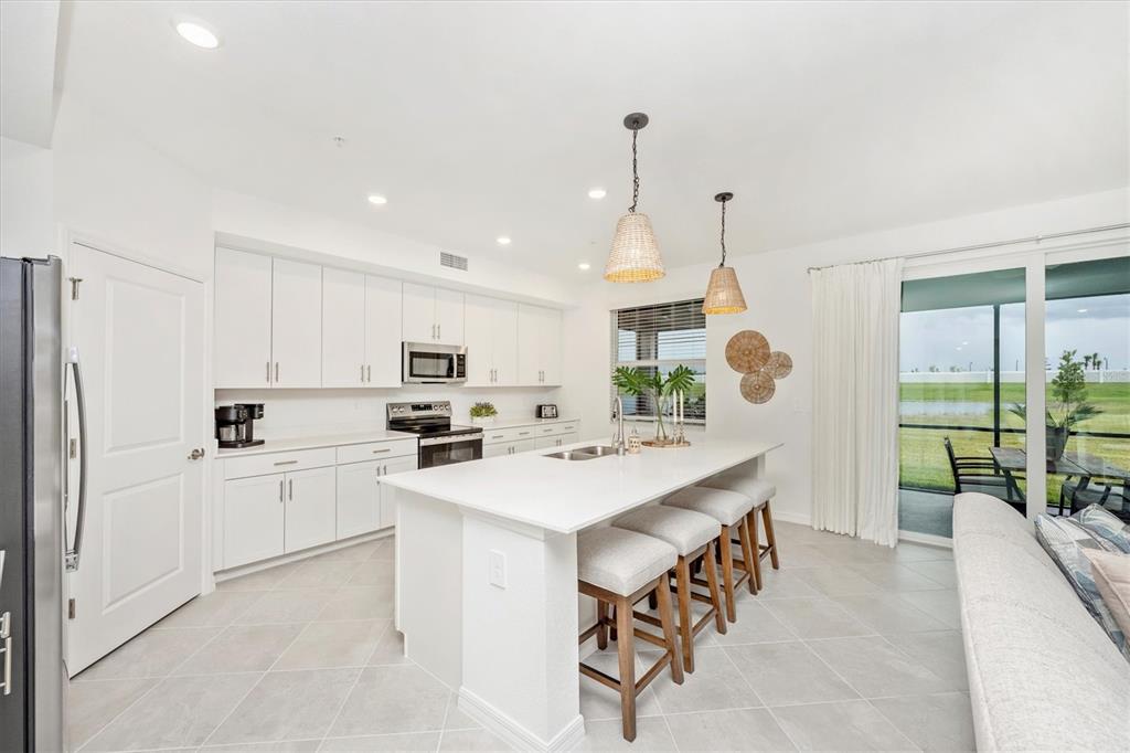 A white kitchen features a central island with bar seating and a view of a patio — 12620 RADIANCE COURT UNIT 101, VENICE, FL