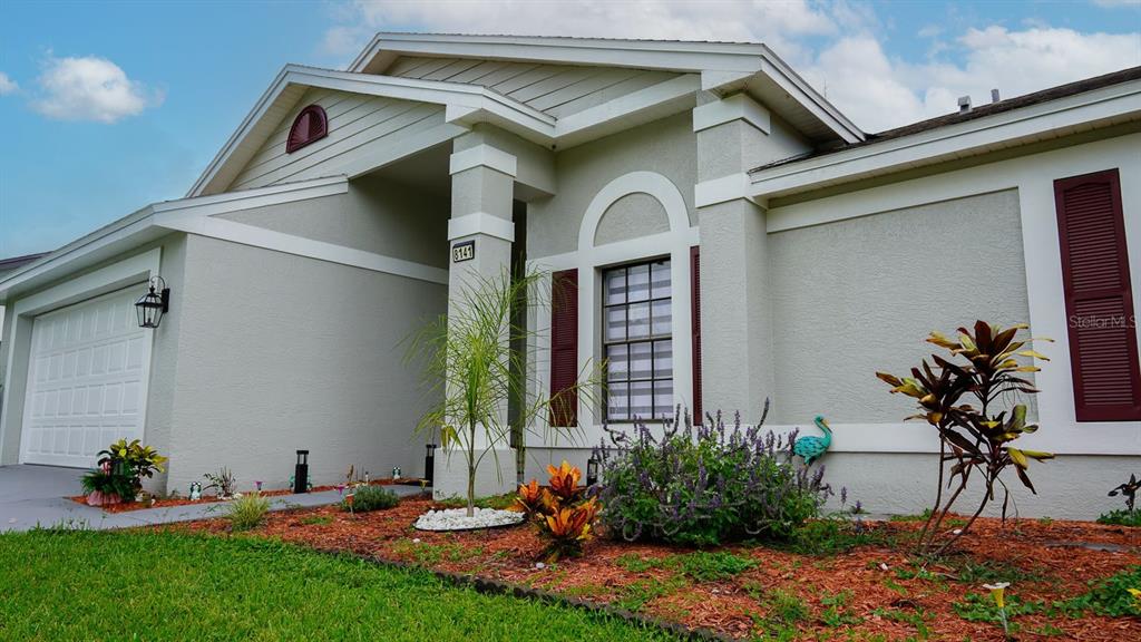 A light-colored house exterior features a garage, a front entrance, and a landscaped garden bed — 8141 GOLF CLUB COURT, HUDSON, FL