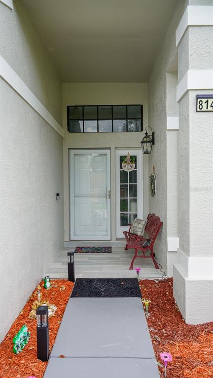 A covered entryway features a front door, a side light, a red bench, and landscaping — 8141 GOLF CLUB COURT, HUDSON, FL