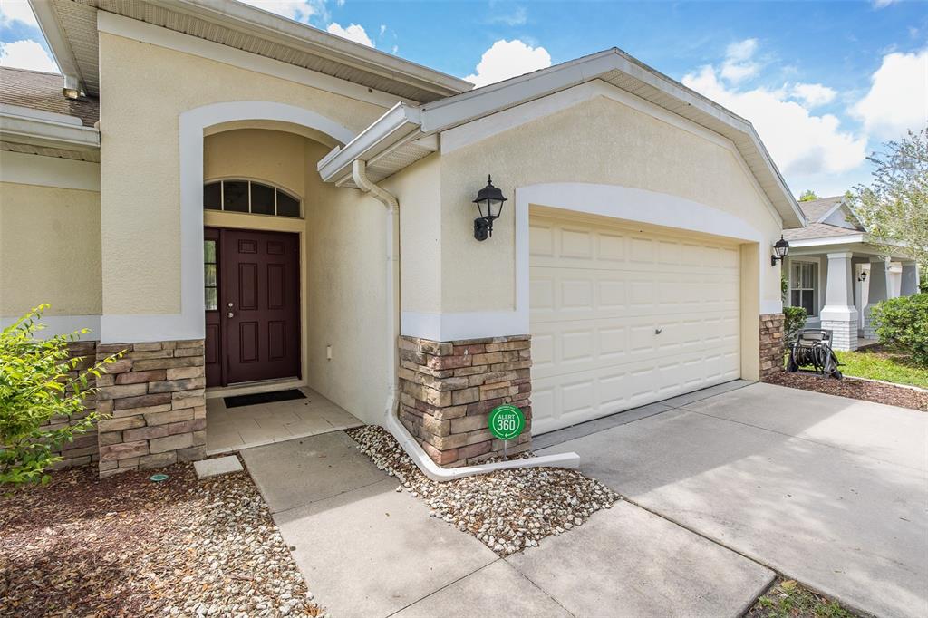 A beige house exterior features a dark brown front door, stone accents, and a garage — 13312 OLD FLORIDA CIRCLE, HUDSON, FL